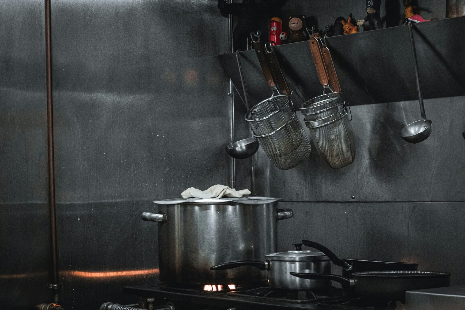 Stainless steel commercial kitchen setup with pots, strainers, and utensils hanging on a rail.