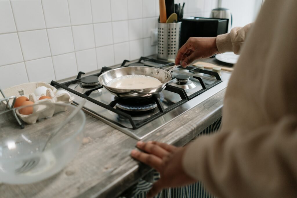 Close-up of omelette cooking on a gas stove in a modern kitchen, highlighting the hands and ingredients.